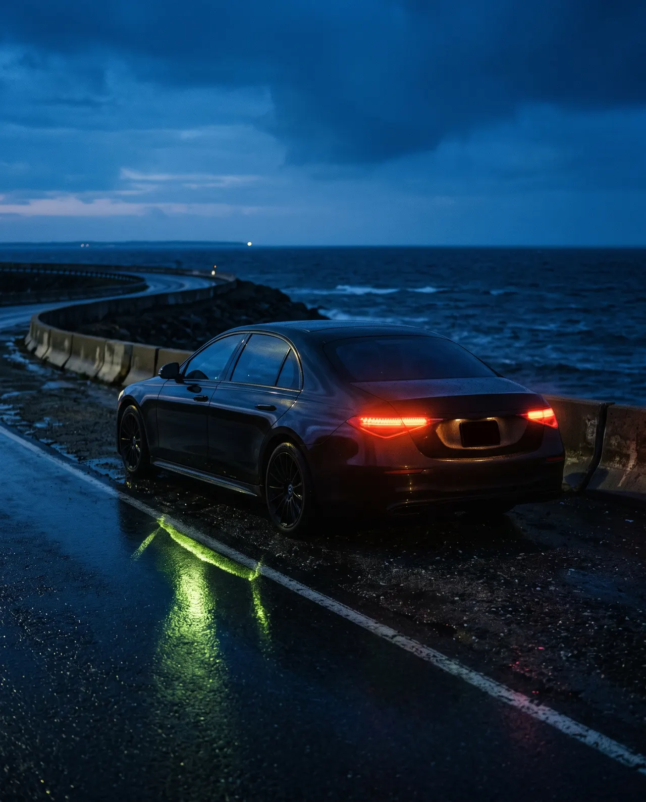 Dark sedan parked on a causeway shoulder at deep blue dusk, ocean behind