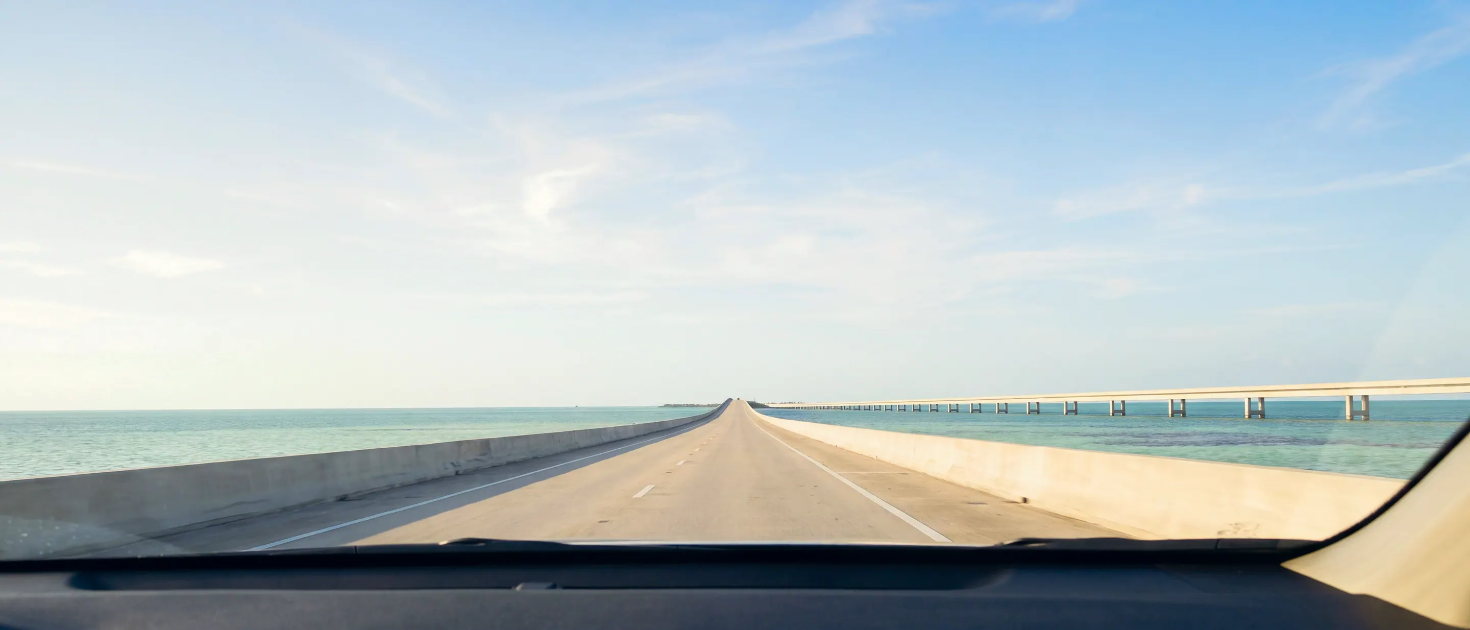 The view through a windscreen: an empty road running ahead between water on both sides